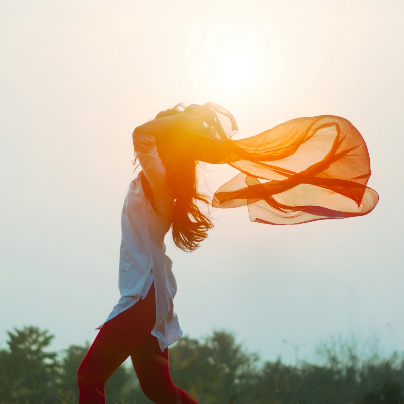 Woman running with scarf blowing in wind with sun behind. Photo by Aditya Saxena on Unsplash