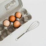 Eggs in carton next to whisk. Photo by Debby Hudson on Unsplash