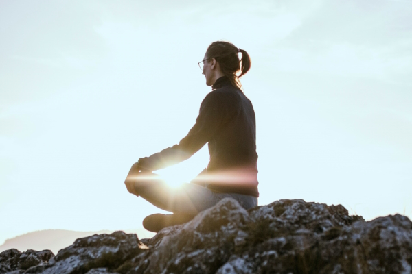 Person sitting atop a rock with sun behind. Photo by Eniko Kis on Unsplash.