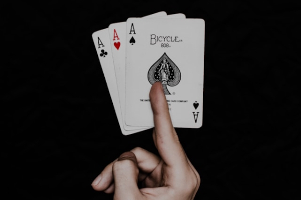 Hand holding three aces. Photo by Klim Musalimov on Unsplash