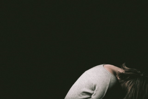 Dark background with person hunched over in foreground. Photo by Malicki M. Beser on Unsplash