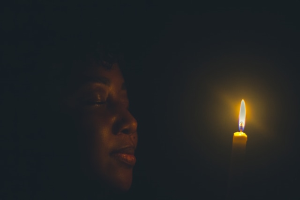 Person facing lit candle flame. Photo by Davino Dove on Unsplash