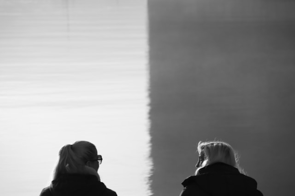Women sitting side by side and talking, one in dark, the other in light. Photo by Giulia Grani on Unsplash.