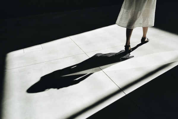 Person walking in pool of light with shadow behind. Photo by Martino Pietropoli on Unsplash