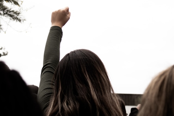 Person in crowd with fist raised toward the sky. Photo by Daniel Ramos on Unsplash