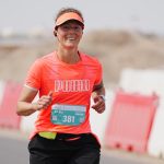 Woman running marathon near barriers and sand dunes
